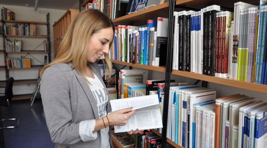 Frau steht vor Bücherregal mit aufgeschlagenem Buch